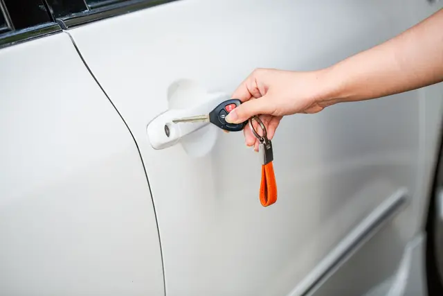 A hand unlocking a white car door with a key and key fob