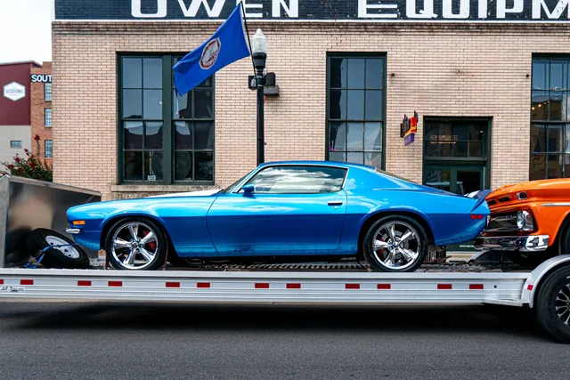 A classic blue Camaro strapped onto a car-hauler trailer