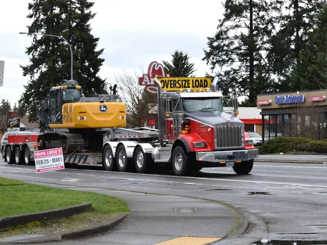 A heavy hauler truck carrying an excavator on a lowboy trailer under an oversize load sign