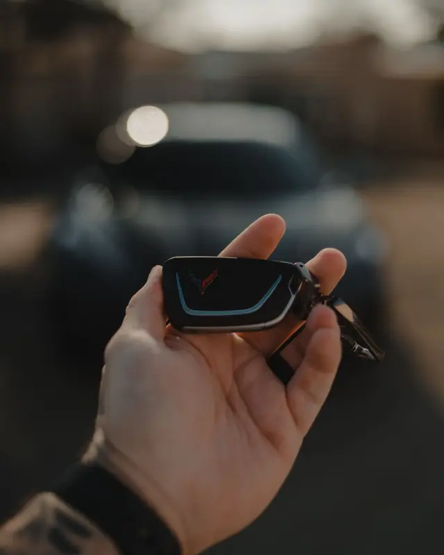A hand holding a car key fob with a car blurred in the background