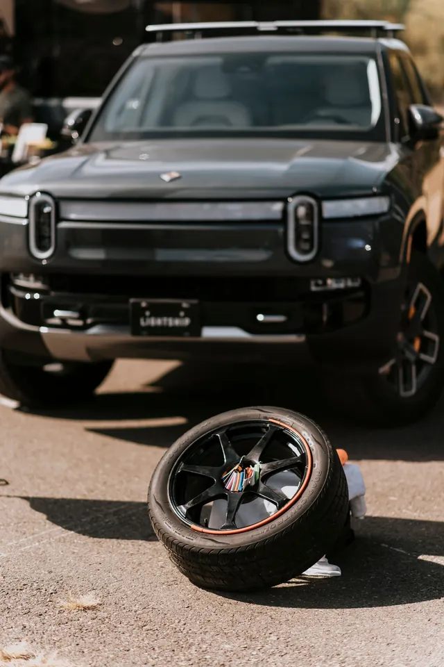 An electric pickup parked on a city street with one wheel removed and the tire on the ground