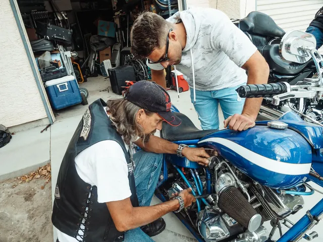 Two men working on the engine of a blue motorcycle in a garage