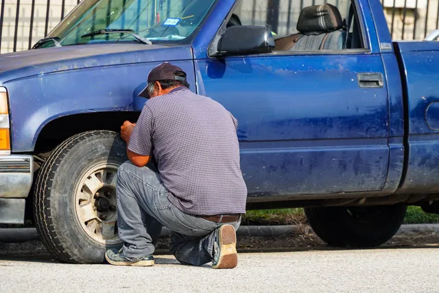 A man kneeling beside a blue pickup truck, working on its flat front tire