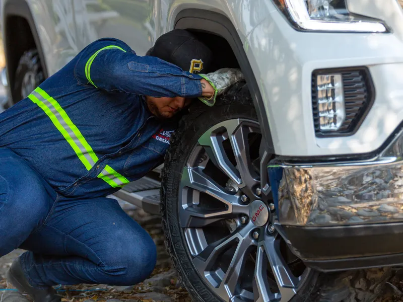 Roadside technician in hi-vis workwear changing the front wheel of a white GMC pickup